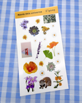 Sheet of nature-themed stickers with flowers and a raccoon on a blue checkered background.